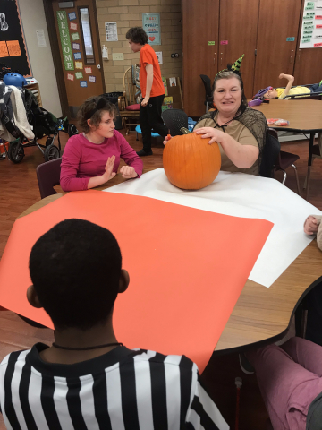 teacher and child sitting next to pumpkin