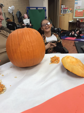 child sitting next to pumpkin